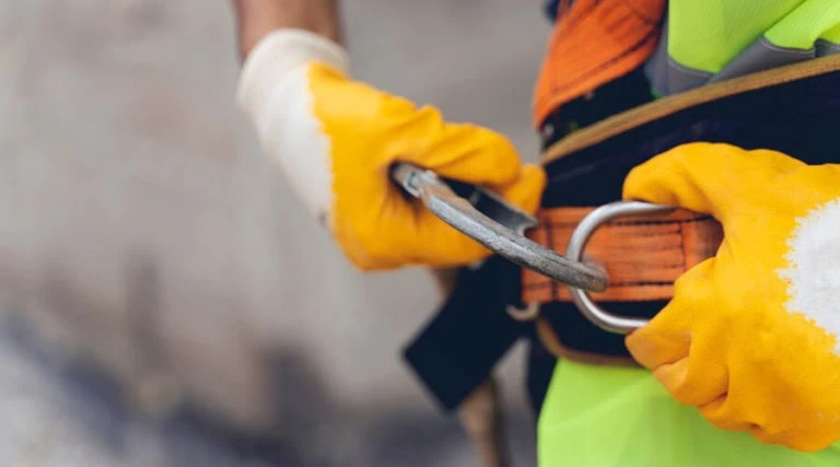 Construction worker adjusts harness for working at heights. A SWMS is required by construction workers when working at heights.