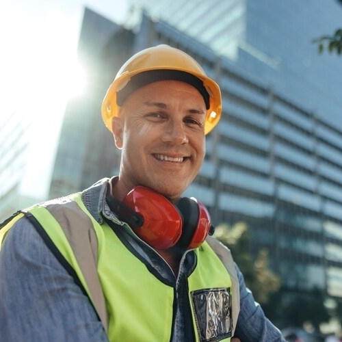 A confident Leading Hand smiles at the camera in front of a completed building.